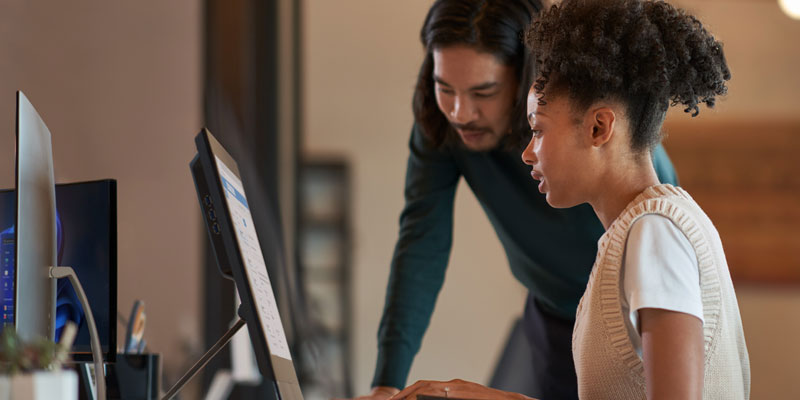 Female office worker on a computer in an office with a male co-worker over her shoulder