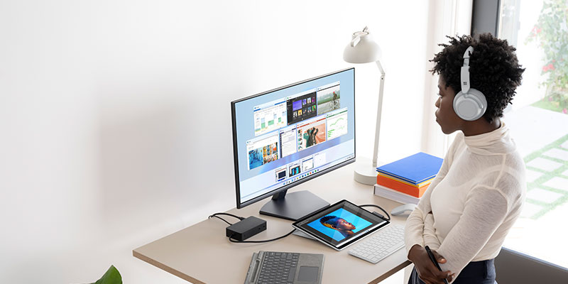 A woman wearing headphones looks at a PC monitor connected to a tablet