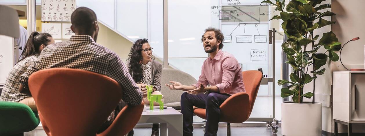 Team members sit around conference table talking.